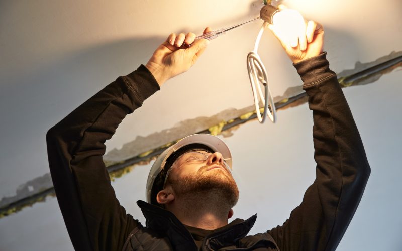 Portrait of male electrician, focused on wiring a temporary light bulb fixture on the ceiling.